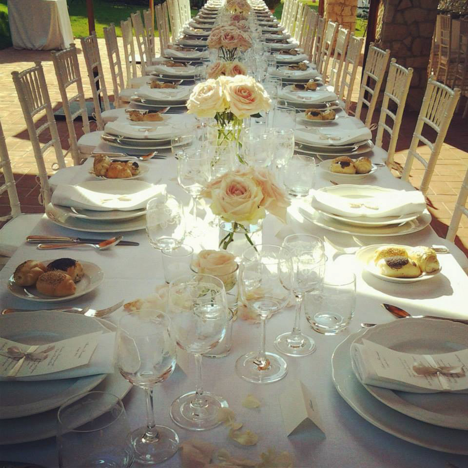 long wedding table with white table cloth and elegant tableware and roses in the middle