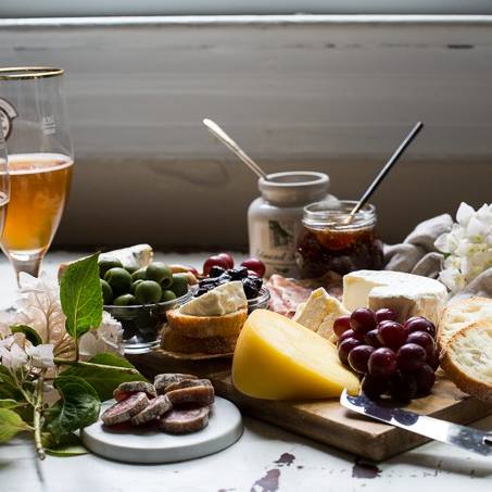 cheese platter with grapes and relish and salami with a glass of beer